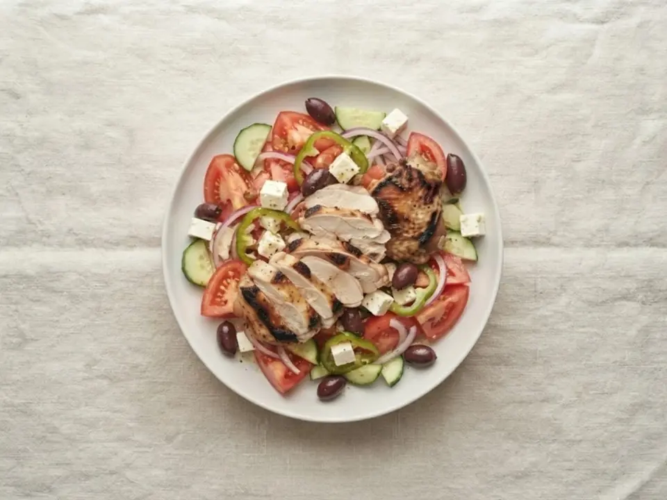 Greek salad with lemon-oregano chicken on a white plate, seen from above